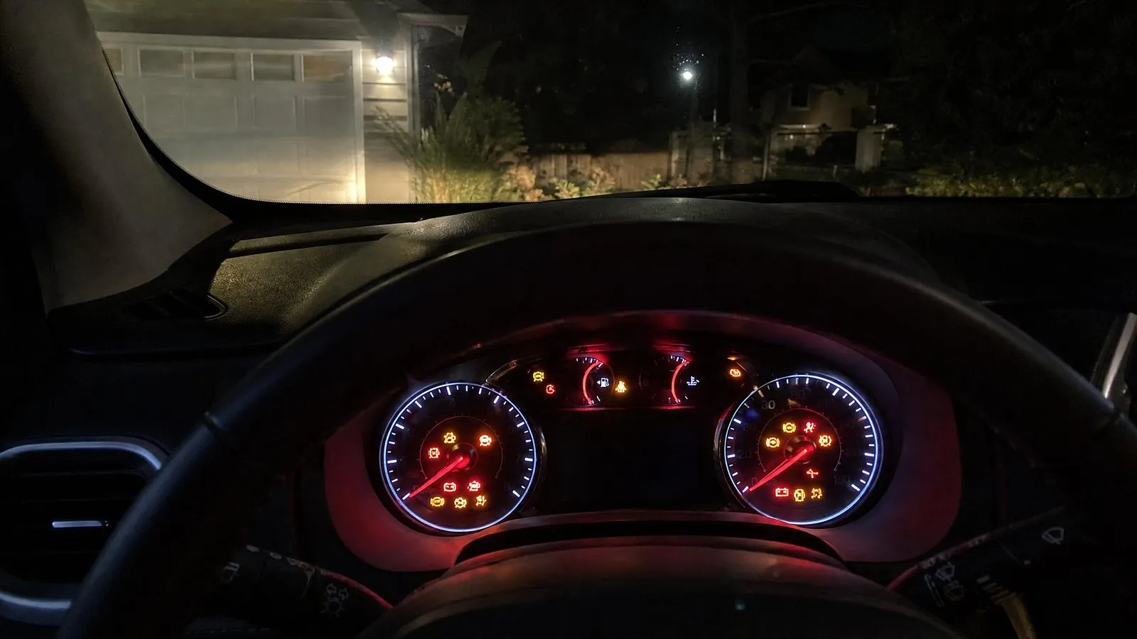 Night view from the driver's seat of an ordinary family car at the moment of ignition, with several dashboard indicator lights glowing, part of the steering wheel in frame and a dark cabin, shot with a realistic phone-camera feel.